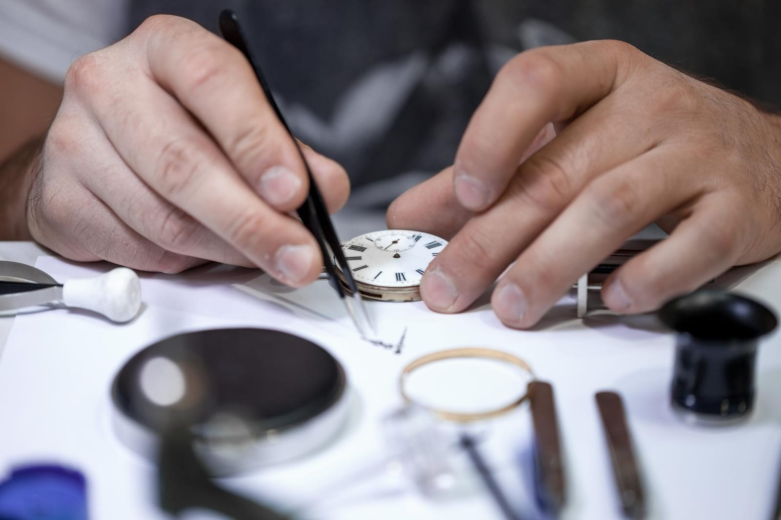 Orologiaio con pinzette e lente d'ingrandimento al lavoro su un quadrante d'epoca